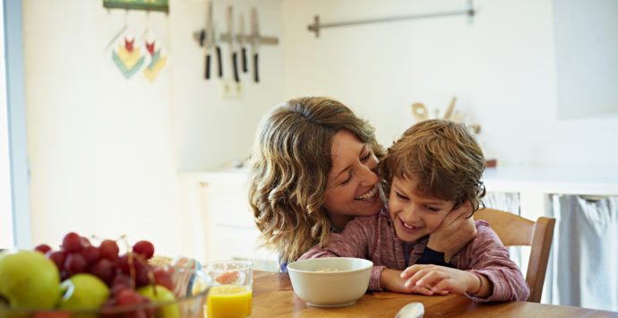 Happy mother embracing son while having breakfast at table in kitchen